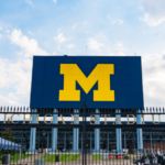 Michigan Stadium exterior with large block “M” sign on scoreboard and entrance gate.