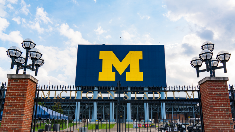 Michigan Stadium exterior with large block “M” sign on scoreboard and entrance gate.